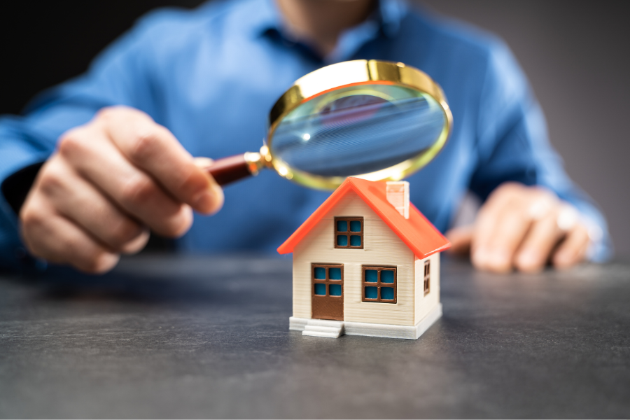 A homeowner closely inspecting a small house with a magnifying glass, symbolizing the careful review of home insurance rates