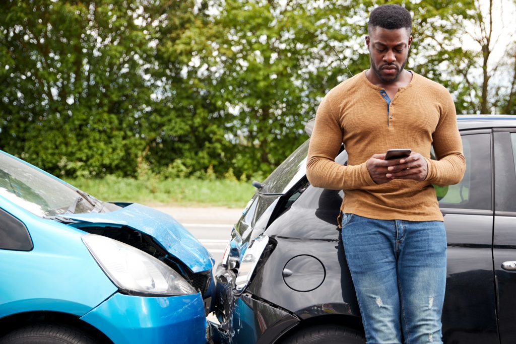 Person on a phone leaning against a car after getting into an accident